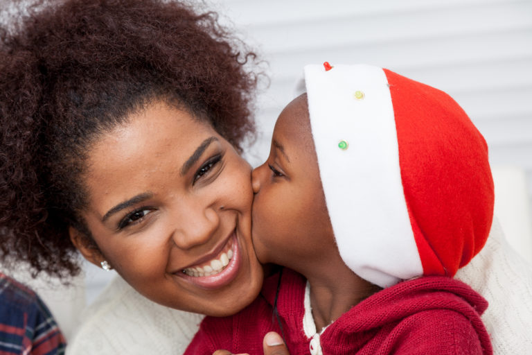 Child in a Santa hat kissing a woman on the cheek