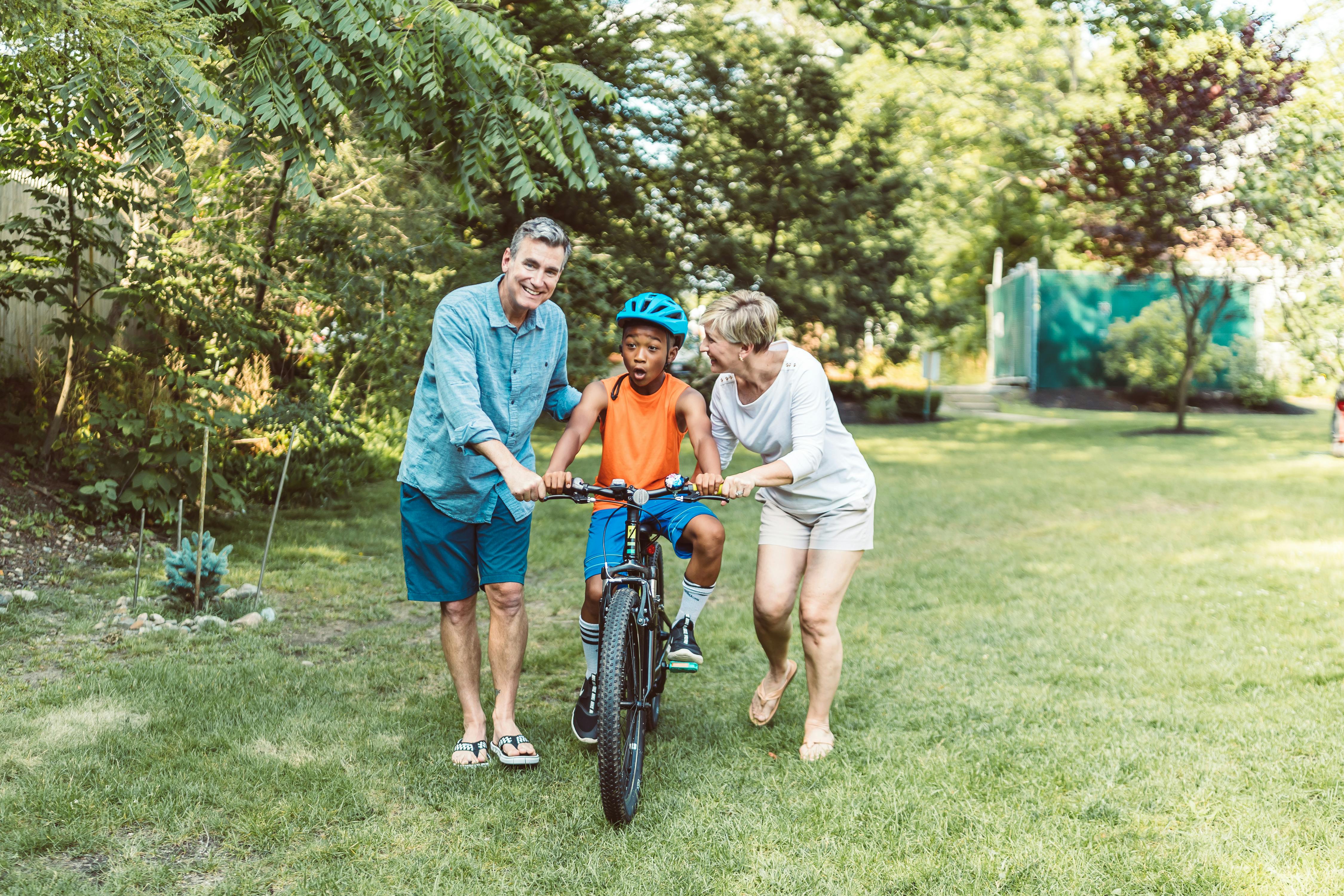 two adults teaching a child to ride a bicycle