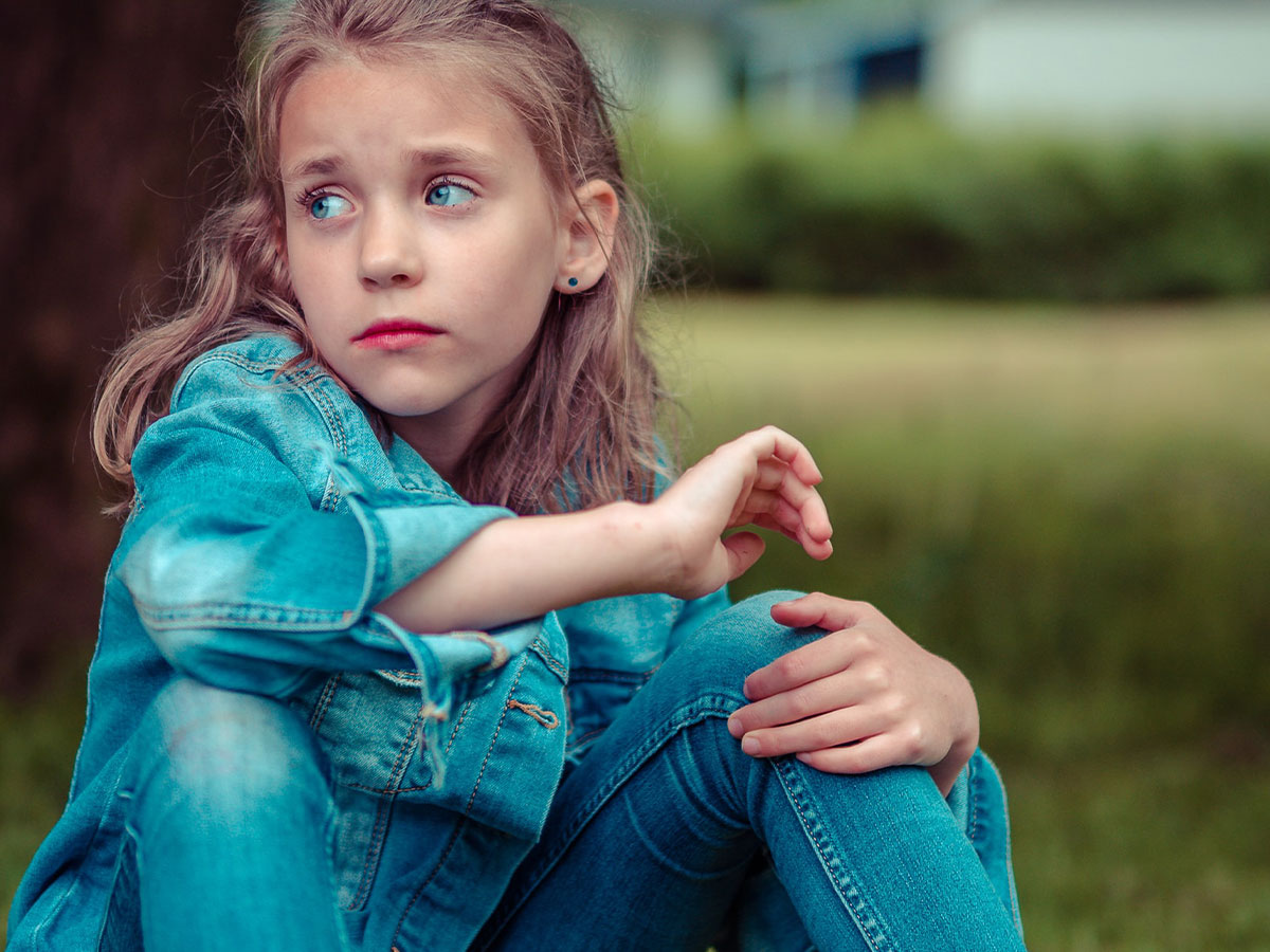A young girl wearing jeans sitting in the grass