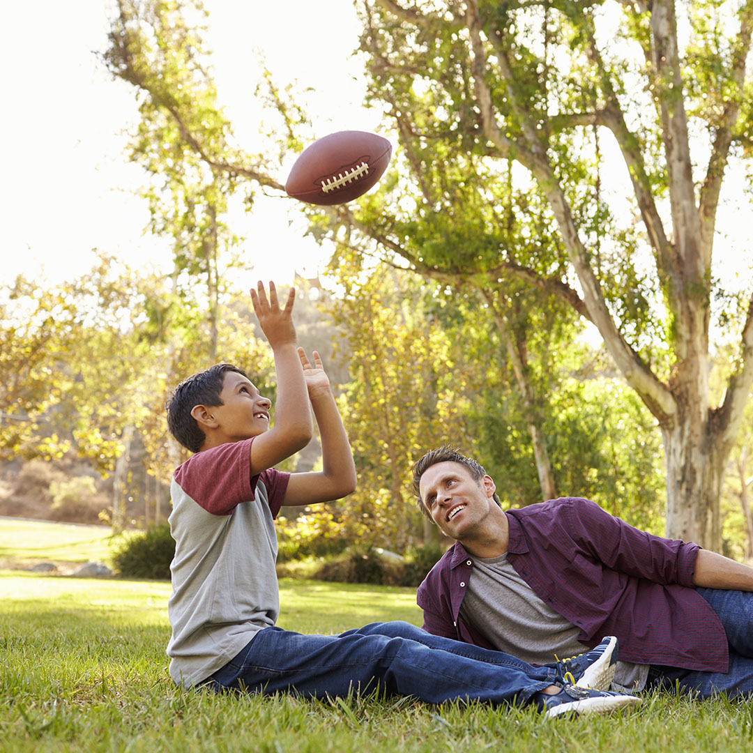 foster son and dad talking in park while throwing a ball