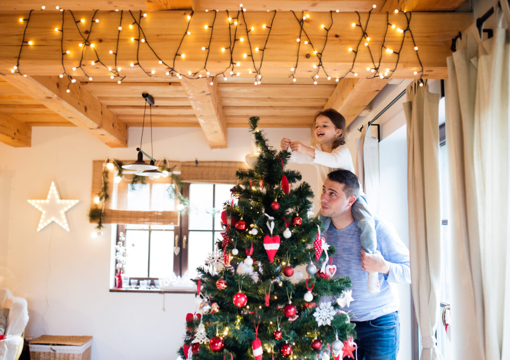 father giving daughter piggyback ride to decorate Christmas tree