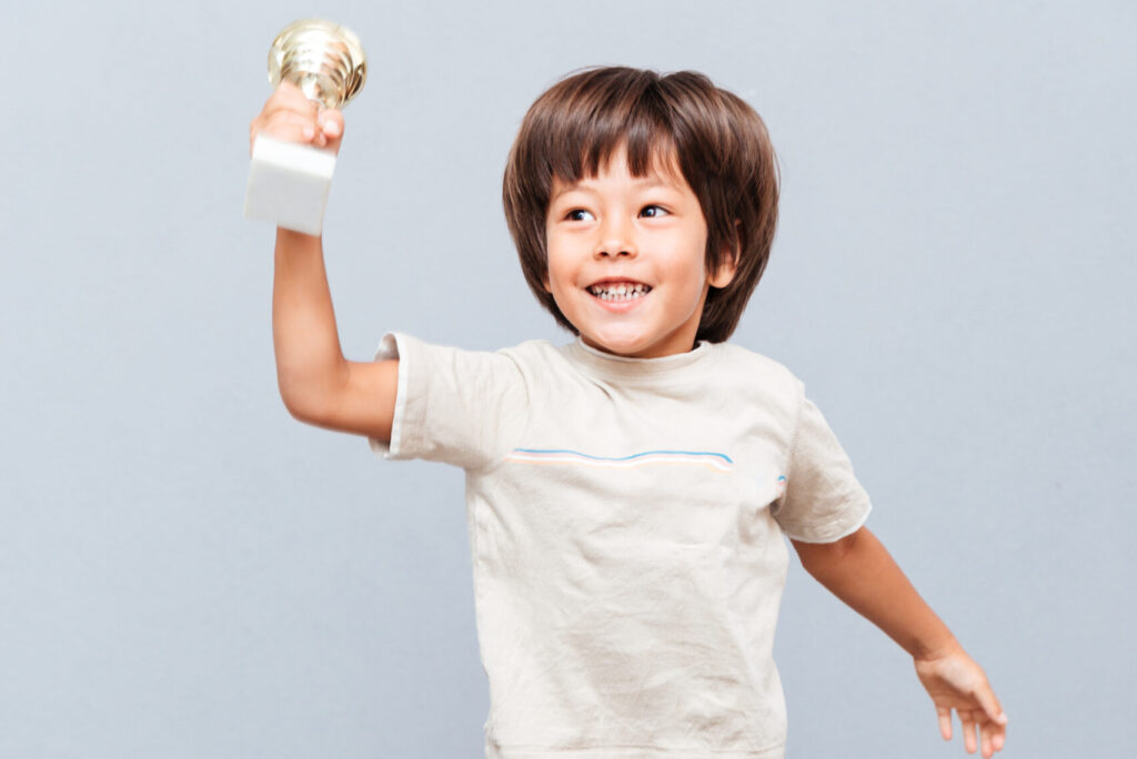 Cheerful little boy cup trophy jumping and laughing over gray background
